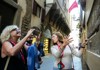 A group walks through a narrow, picturesque street in Florence, with historic buildings and colorful flags lining the path.