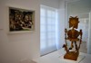 A collection of Picasso's works displayed in a bright gallery space, with a visitor admiring a sculptural piece.